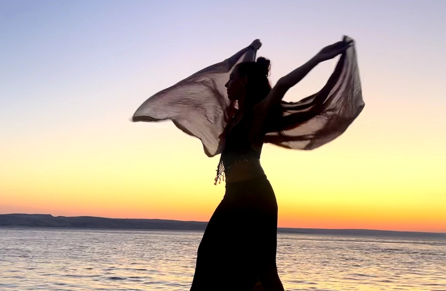 a woman standing on a beach with a scarf in her hands